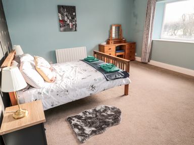 A bedroom with a bed towels on it a lamp on a bedside table a dressing table and a window at Moorlaws Farm in Alnwick