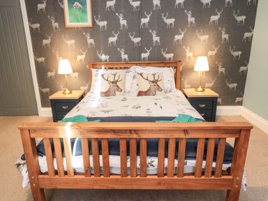 A bedroom with a wooden bed frame two bedside tables with lamps and deer patterned wallpaper at Moorlaws Farm in Alnwick
