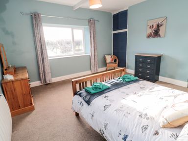 A bedroom with a wooden bed a chest of drawers a wicker chair blue wardrobes and a window with curtains at Moorlaws Farm in Alnwick