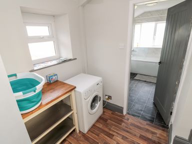A laundry room with a washing machine a small shelving unit and a collapsible basin next to a window at Moorlaws Farm in Alnwick
