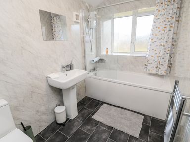 A bathroom with a sink, bathtub, showerhead, mirror, window with curtain, and toilet at Moorlaws Farm in Alnwick