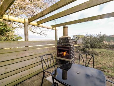 An outdoor seating area with a black glass table and two metal chairs next to a brick fireplace at Moorlaws Farm in Alnwick