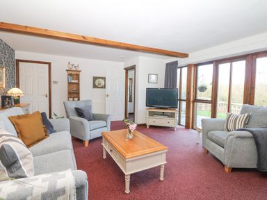 A living room with sofas armchairs a coffee table TV and large windows at Woodland View in Muddiford near West Down