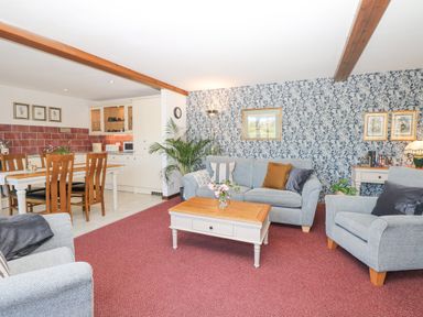 A living room with blue sofas table and wooden dining table and kitchen area at Woodland View in Muddiford near West Down