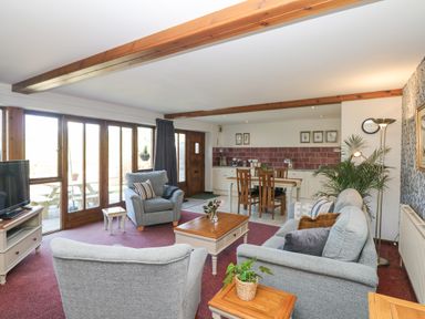 A living room with armchairs coffee table dining table and large windows at Woodland View in Muddiford near West Down