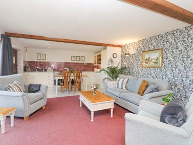 An open plan living room and kitchen with sofas, coffee table, dining table, and patterned wallpaper at Woodland View in Muddiford near West Down