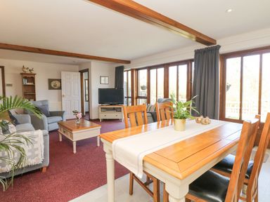 A dining area with a wooden table and chairs next to a living room with armchairs and a coffee table at Woodland View in Muddiford near West Down