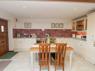 A kitchen with a wooden dining table and chairs and white cabinets at Woodland View in Muddiford near West Down