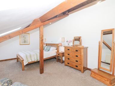 A bedroom with wooden bed frame side table chest of drawers and full length mirror at Woodland View in Muddiford near West Down