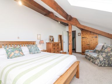 A bedroom with a wooden bed a dresser a standing mirror a floral patterned sofa and exposed wooden beams at Woodland View in Muddiford near West Down