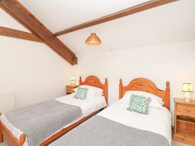 A bedroom with two wooden single beds side by side each with white bedding green patterned pillows and grey blankets wooden nightstands with green lamps and exposed wooden ceiling beams at Woodland View in Muddiford near West Down