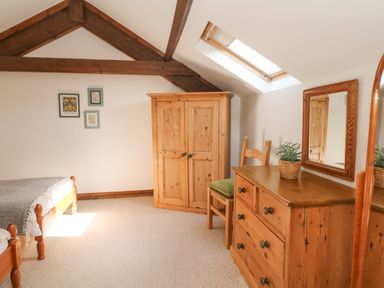 A bedroom with wooden furniture including a dresser with a mirror, a chair, a wardrobe, and a bed at Woodland View in Muddiford near West Down