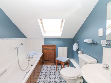 A bathroom with a bathtub shower toilet sink wooden stool skylight window and blue walls at Woodland View in Muddiford near West Down