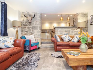 A living room with leather sofas a wooden coffee table and a stone wall with a skull mounted at La Petit Maison in St Columb Major
