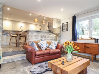 A living room with a leather sofa and wooden coffee table next to an open kitchen at La Petit Maison in St Columb Major