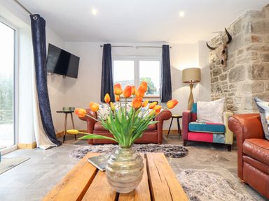 A living room with orange flowers on a wooden coffee table and leather sofas at La Petit Maison in St Columb Major