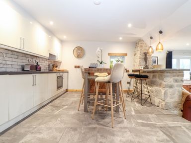 A kitchen with a dining table and chairs a stone bar with stools and a clock on the wall at La Petit Maison St Columb Major