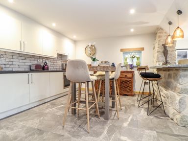 A kitchen with white cabinets a dining table with chairs and a stone breakfast bar at La Petit Maison in St Columb Major