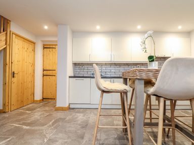 A kitchen with white cabinets stone floor wooden doors and light-colored chairs at La Petit Maison in St Columb Major