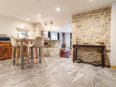 A kitchen and dining area with stone walls a bar counter with pendant lights and stools and a wooden table with chairs at La Petit Maison in St Columb Major