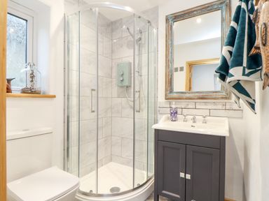 A bathroom with a corner shower, toilet, sink with cabinet, mirror, and towels at La Petit Maison in St Columb Major