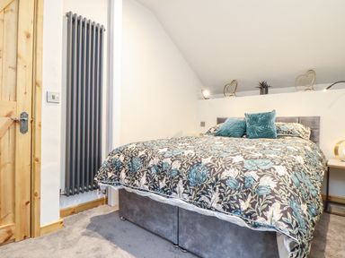 A bedroom with a bed covered with a floral patterned duvet and teal pillows by a wooden door and a vertical radiator at La Petit Maison in St Columb Major