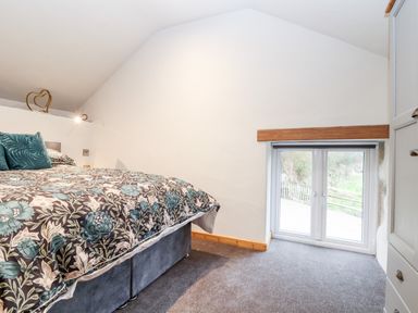A bedroom with a bed and floral bedding near a window and white walls at La Petit Maison in St Columb Major