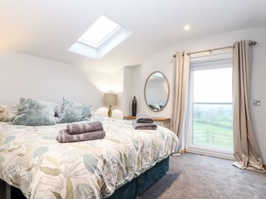 A bedroom with a bed with pillows and towels a lamp a mirror and a window with curtains at La Petit Maison in St Columb Major