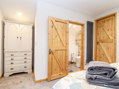 A bedroom with wooden doors a white wardrobe and folded towels on a bed at La Petit Maison in St Columb Major