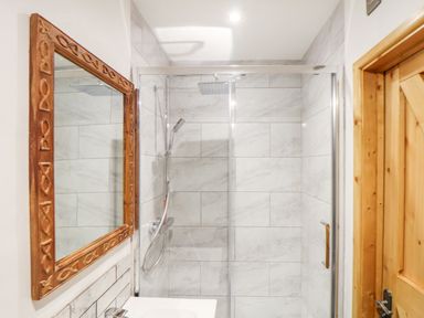 A bathroom with a glass shower enclosure white tiled walls a wooden framed mirror and a wooden door at La Petit Maison in St Columb Major