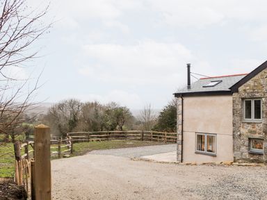 Side view of a house with stone and plaster walls next to a gravel driveway and wooden fence at La Petit Maison in St Columb Major