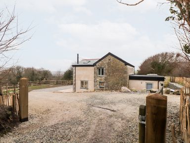 A stone and plaster house with fenced gravel driveway and surrounding trees at La Petit Maison in St Columb Major