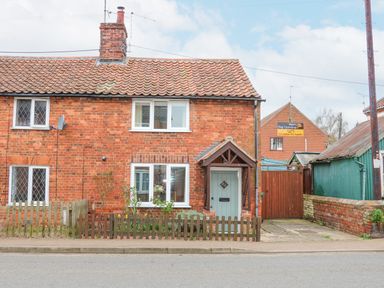 A brick house with a tiled roof and a small front garden behind a wooden fence at Easter Cottage in Dersingham
