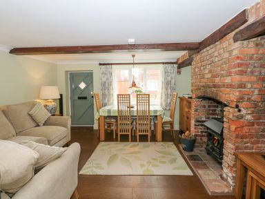 A living room with sofas a dining table a brick fireplace and wooden beams at Easter Cottage in Dersingham