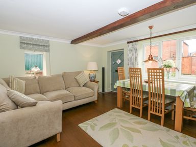 A living room with a beige sofa a wooden dining table with chairs and a lamp at Easter Cottage in Dersingham