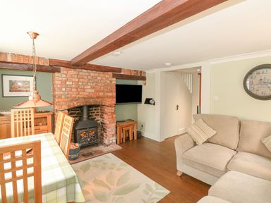 A living room with a brick fireplace, wood-burning stove, dining table with chairs, and a beige sofa at Easter Cottage in Dersingham