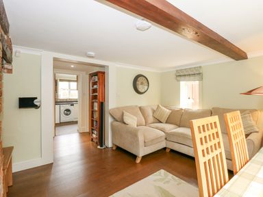 A living room with a beige corner sofa a wooden dining table and chairs wooden floor and a bookshelf at Easter Cottage in Dersingham