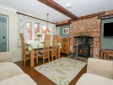 A dining room with a wooden table and chairs a fireplace and a window at Easter Cottage in Dersingham