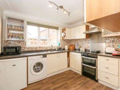 A kitchen with white cabinets a black oven a washing machine a microwave and a window at Easter Cottage in Dersingham