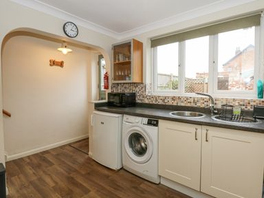 A kitchen area with a washing machine refrigerator and sink under a window at Easter Cottage in Dersingham