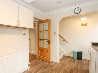 A kitchen area with wooden floor a glass-paneled wooden door a staircase with handrail and two trash bins at Easter Cottage in Dersingham