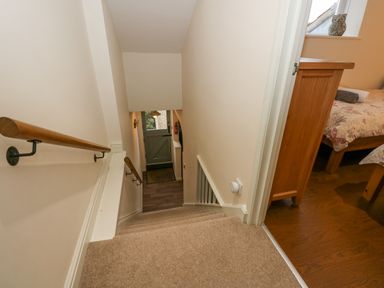 A stairway with wooden handrails leading down to a door and a bedroom with wooden bed frame and floral bedding at Easter Cottage in Dersingham