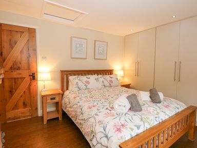 A bedroom with a wooden bed with floral bedding two bedside tables with lamps a wooden door and built-in wardrobes at Easter Cottage in Dersingham