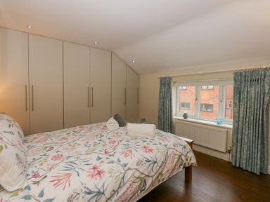 A bedroom with floral bedspread large wardrobe and window with blue curtains at Easter Cottage in Dersingham