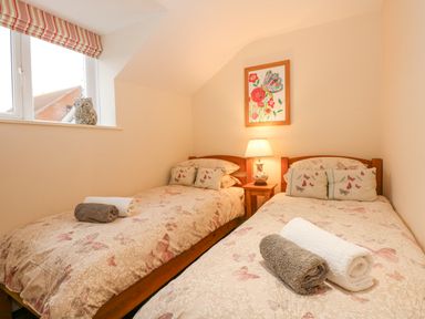 A twin bedroom with two beds with butterfly bedding a bedside table with a lamp and a window with a decorative owl at Easter Cottage in Dersingham