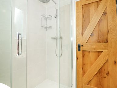 A bathroom shower with glass door and metal shower fixtures next to a wooden door at Easter Cottage in Dersingham