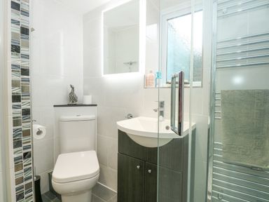 A bathroom with a toilet sink with cabinet a mirror and a glass shower door at Easter Cottage in Dersingham