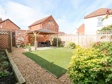 A backyard garden with a wooden pergola and outdoor furniture at Easter Cottage in Dersingham