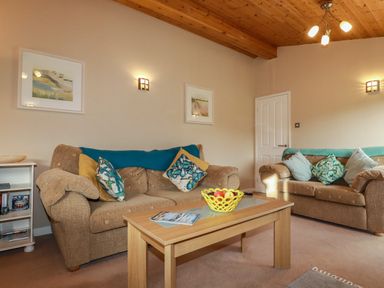 A living room with two beige sofas and a wooden coffee table with a fruit bowl and magazines at 4 The Glade in St Minver