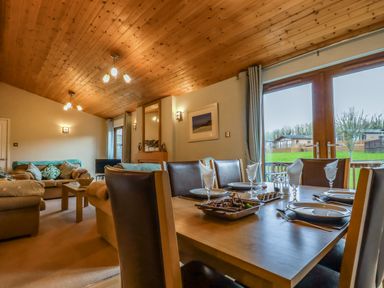 A dining table set with plates and glasses next to a living room with sofas and a wooden ceiling at 4 The Glade in St Minver